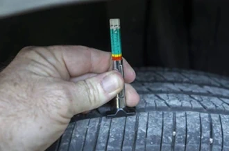 A man is checking tire tread depth with a color-coded tread depth gauge