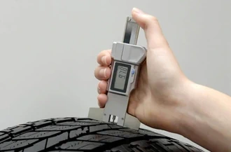A man is checking tire tread depth with a digital tread depth gauge