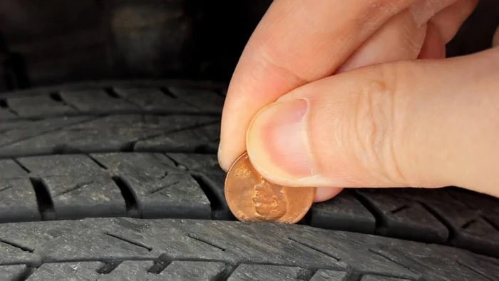A man is performing the penny test for checking the tire tread depth