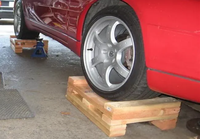 Wooden blocks beneath a red car's tires to prevent flat spot